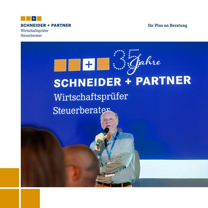 Ein Mann spricht in ein Mikrofon, hinter ihm ist auf einer Leinwand ein Firmenlogo zu sehen.