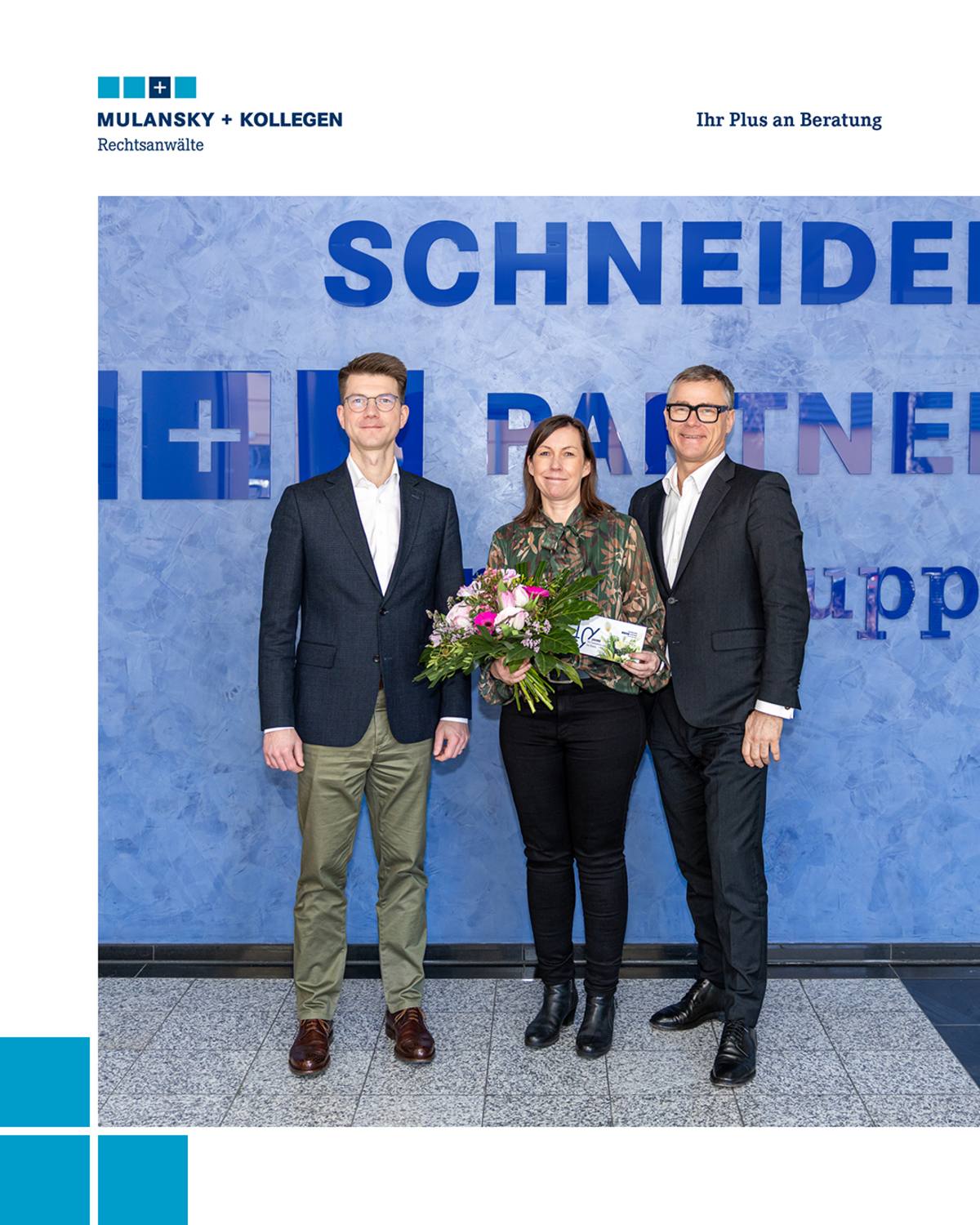 Zwei Männer stehen links und rechts von einer Frau, die einen Blumenstrauß hält.